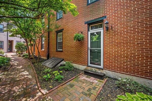 A brick building with a door, windows, and a small garden area with plants and a pathway. - Quiet Fells Point Home Just off the Main Street (Baltimore)