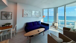 Un salon moderne avec un canapé bleu, une table basse en bois et une vue sur l’océan grâce à de grandes fenêtres.