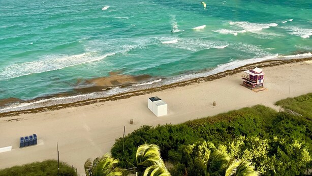Une plage avec une tour de surveillance pour les sauveteurs, un bâtiment blanc et un arc-en-ciel au-dessus de l’océan.