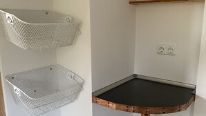 A corner with a metal basket shelf, a small table with a black top, and a shelf with a first aid kit and a box labeled "Medicines & Bandages".