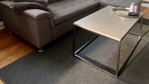 A modern living room with a grey sectional sofa, a glass coffee table, and a grey rug.