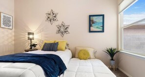 A bedroom with a bed, a nightstand, a lamp, wall art, a window, and a plant.