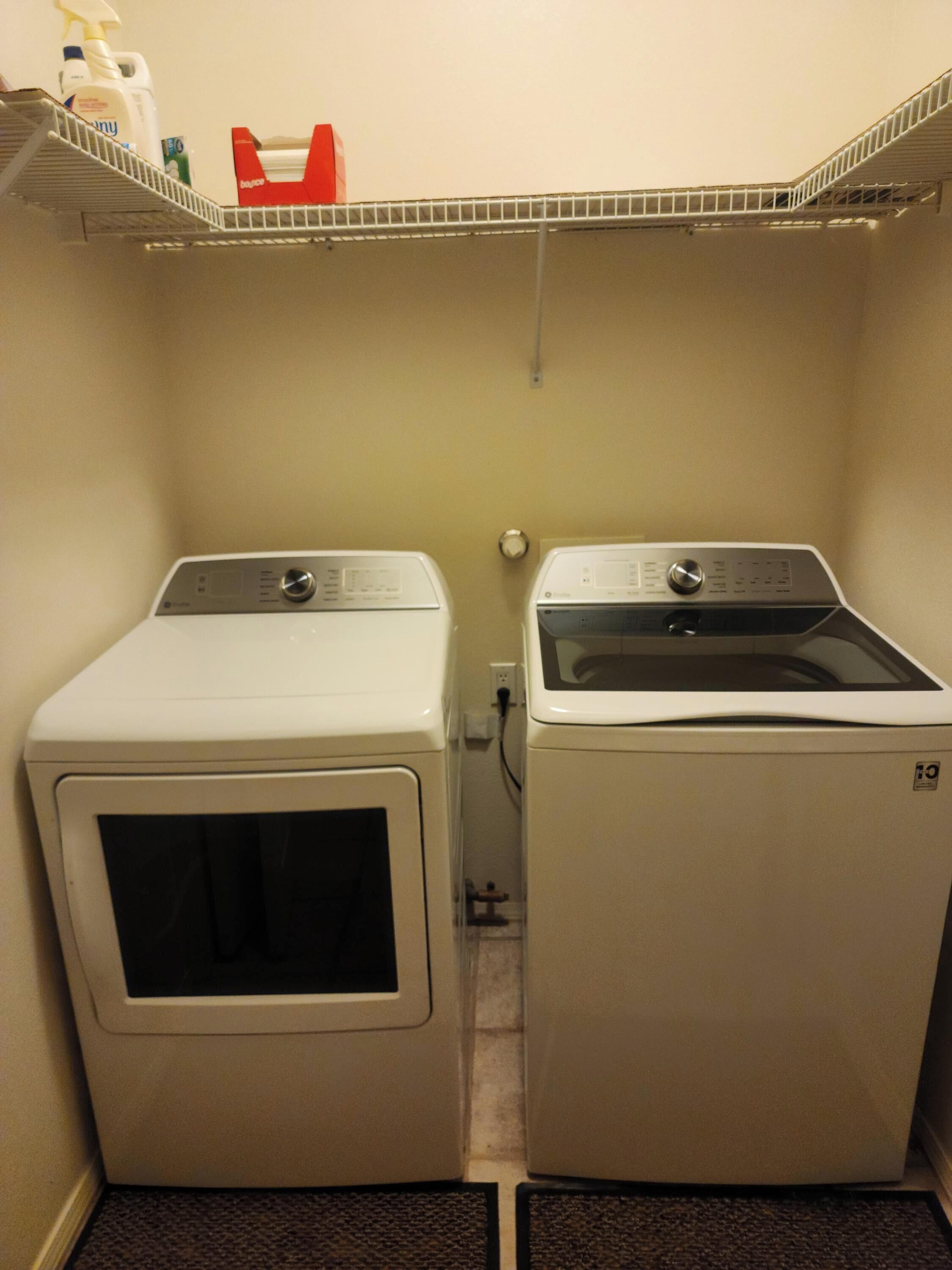 A laundry room with two front-loading washing machines and a shelf above them.