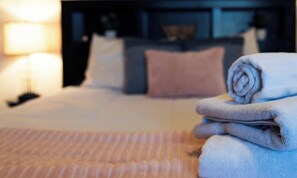 A neatly made bed with a rolled-up towel on the side, a lamp, and a nightstand.