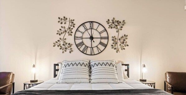 Ein Schlafzimmer mit einem Bett, zwei Nachttischen, einer Wanduhr und Zimmerpflanzen.
