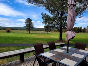 A deck with a table and chairs, overlooking a grassy field with trees and a mountain in the distance.