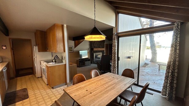 A compact kitchen with wooden cabinets, a dining table with chairs, and a large sliding glass door leading to an outdoor area. - Cozy Sunriver Cabin with Access to Exclusive Golf (Sunriver)