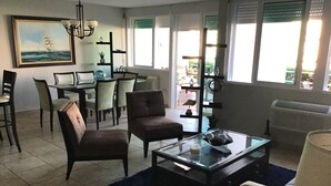A living room with a dining area, a chandelier, a painting, and a view through the windows. - 3 Bedrooms Apt. close to main beaches/ attractions (Río Grande)