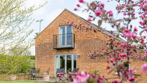 Une maison en briques avec un balcon, une porte-fenêtre coulissante et une petite terrasse aménagée avec du mobilier d’extérieur.