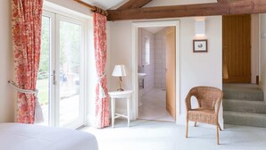 Une chambre à coucher avec un lit, une chaise, une table avec une lampe, et une salle de bain visible à travers une porte ouverte.