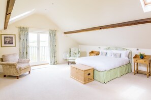 A bedroom with a large bed, a chair, a wooden chest, and a window with curtains. - Chater Barn (Leicester)