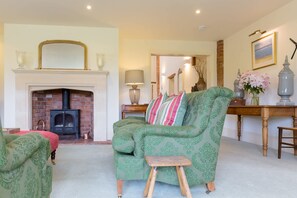 A living room with a fireplace, a green armchair, a wooden stool, and a table with decorative items.