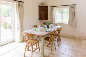 A dining area with a table set for four, surrounded by wooden chairs, a window with curtains, and a door with a curtain.