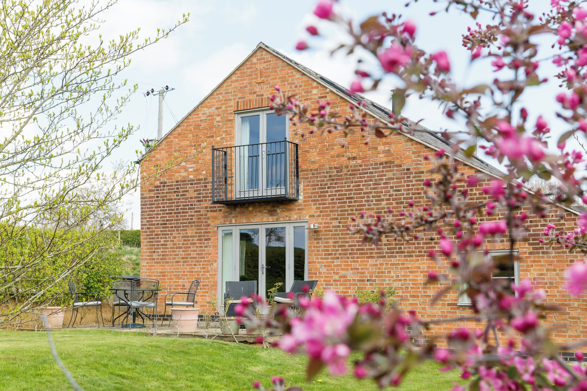 A two-story brick house with a balcony, a patio with outdoor furniture, and a garden.