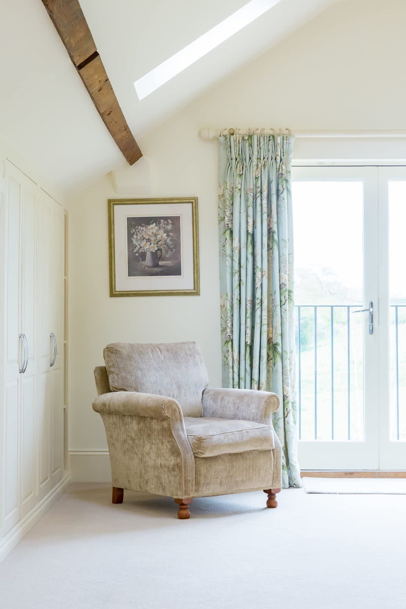 A room with a single armchair, a framed picture on the wall, and a window with floral curtains.