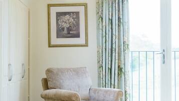 A room with a single armchair, a framed picture on the wall, and a window with floral curtains.