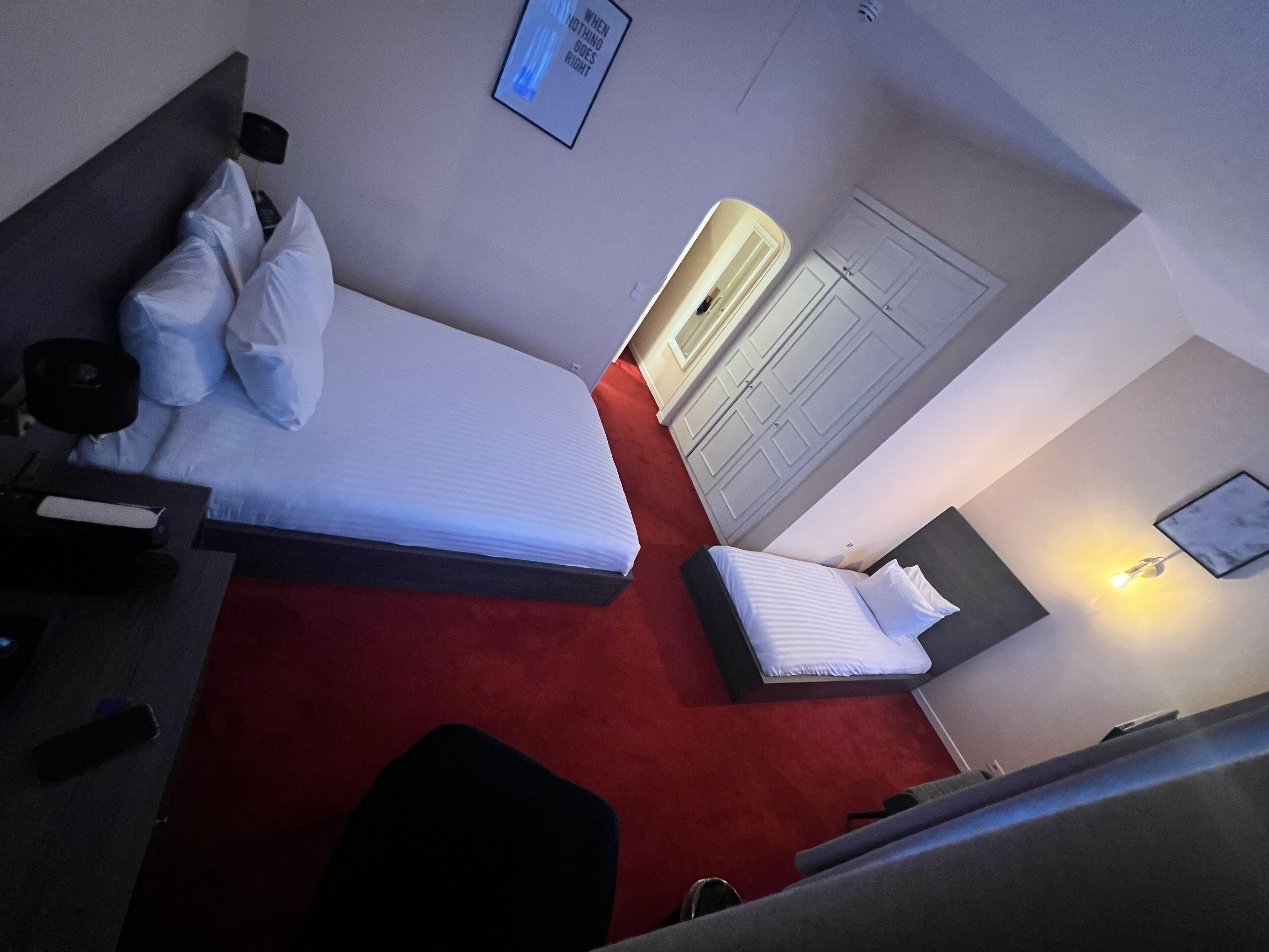Habitación de hotel con cama, escritorio, silla, armario y una lámpara en la pared.