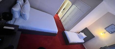 Habitación de hotel con cama, escritorio, silla, armario y una lámpara en la pared.