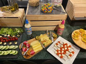 Variedad de alimentos y condimentos sobre una encimera de cocina, incluyendo queso, tomates, pepinos y brochetas.
