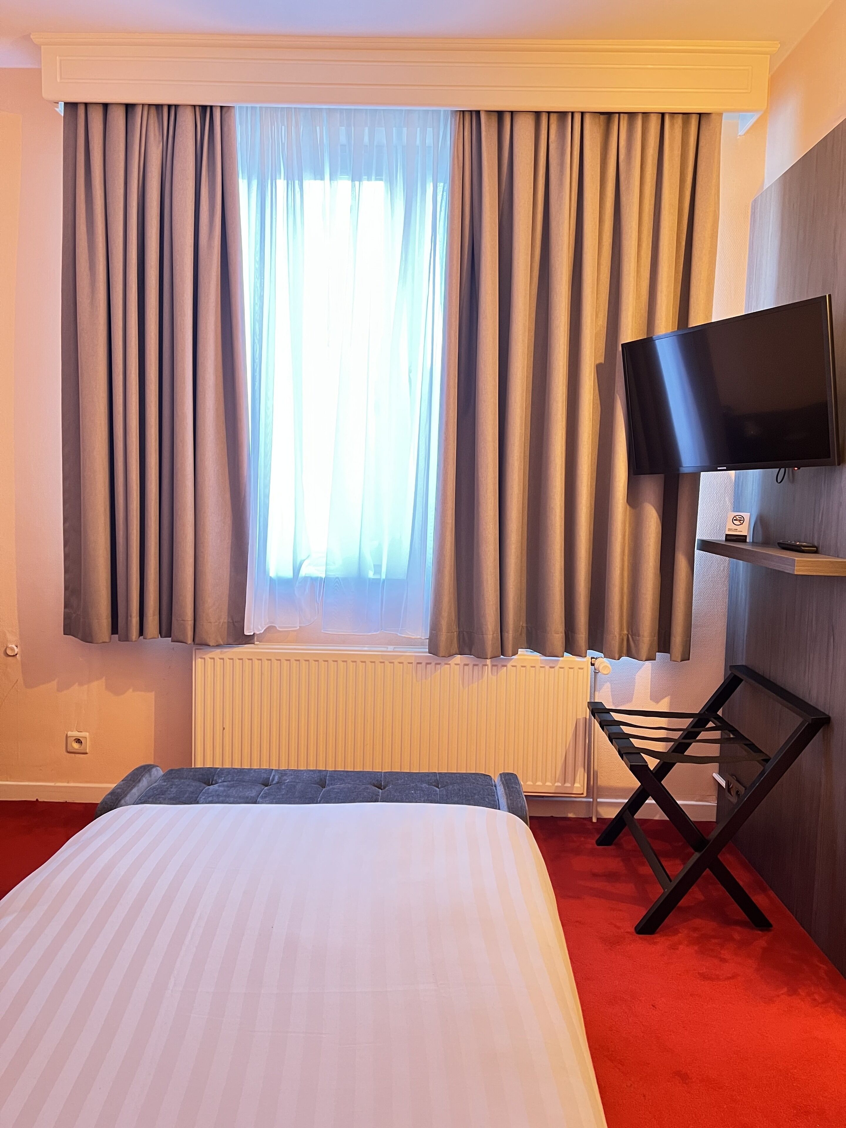 Una habitación de hotel con una cama, un televisor montado en la pared y una ventana con cortinas.