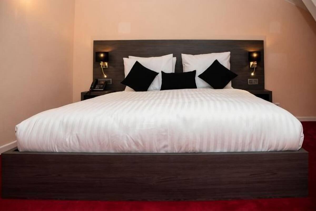 A bed with a dark headboard, white bedding, and black pillows. There are two bedside tables with lamps.