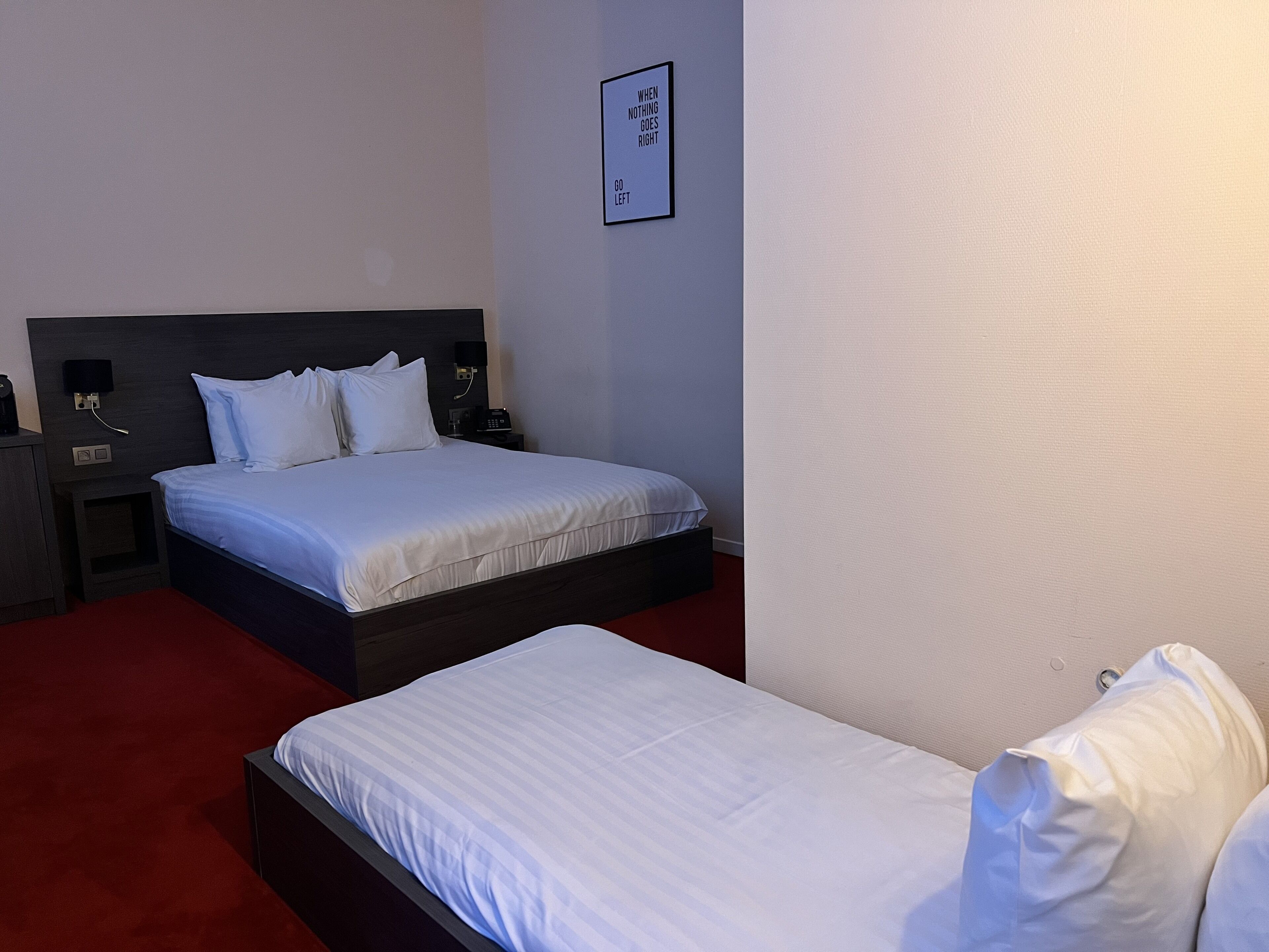 Una camera d'albergo con un letto grande, un letto più piccolo, un comodino con un telefono e un cartello fissato al muro.
