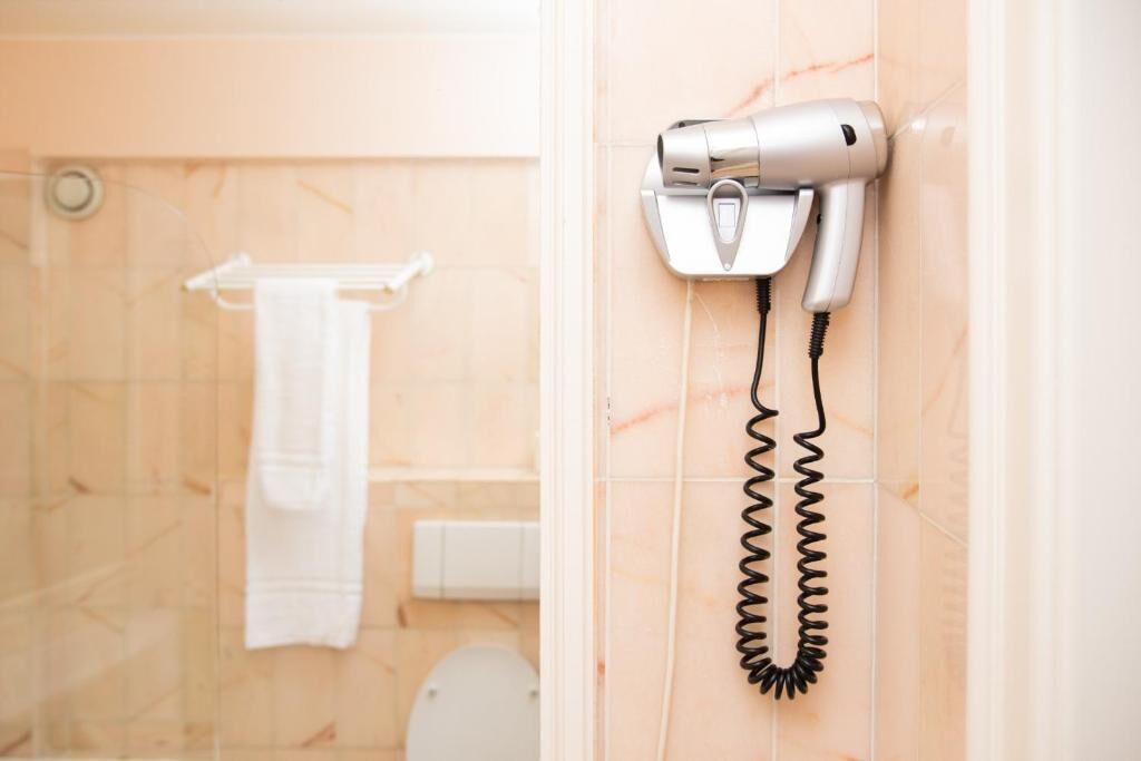 Une salle de bain équipée d’un sèche-cheveux fixé au mur, d’une serviette blanche suspendue à un porte-serviettes et de toilettes.