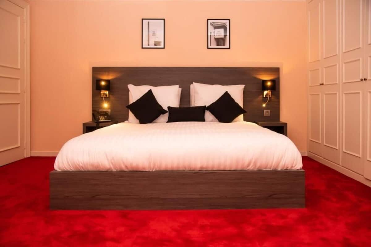 A bedroom with a large bed, two bedside tables, and a red carpet.