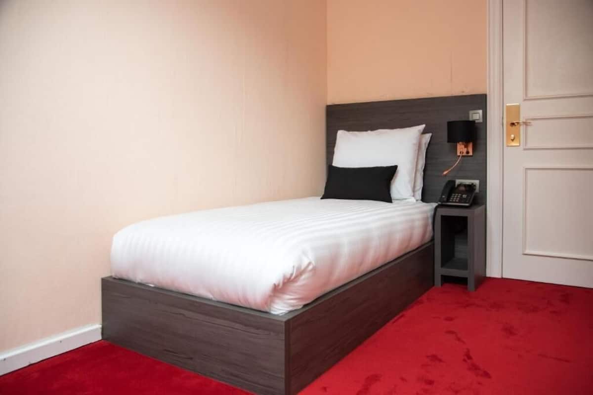 A neatly made bed with a wooden headboard, a bedside telephone, and a red carpeted floor.