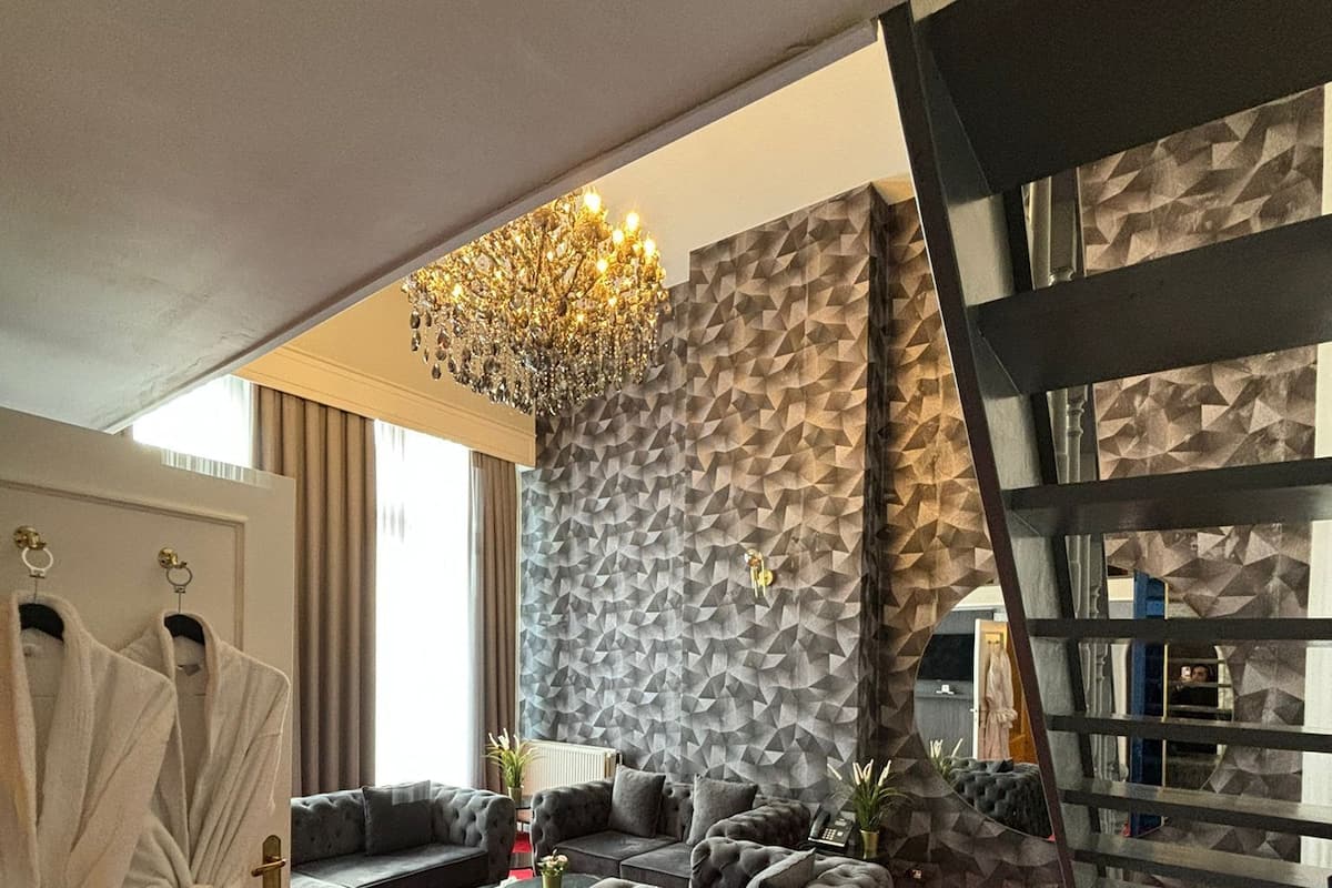 A modern living room with a red carpet, grey sofas, a chandelier, and a geometric wall design.