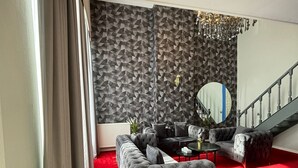 Una sala de estar moderna con alfombra roja, sofás tapizados en gris, un espejo redondo y una escalera.