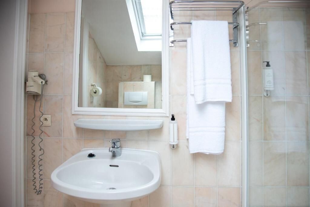Un baño con lavamanos, espejo, toallero y ducha.