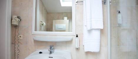 Un baño con lavamanos, espejo, toallero y ducha.