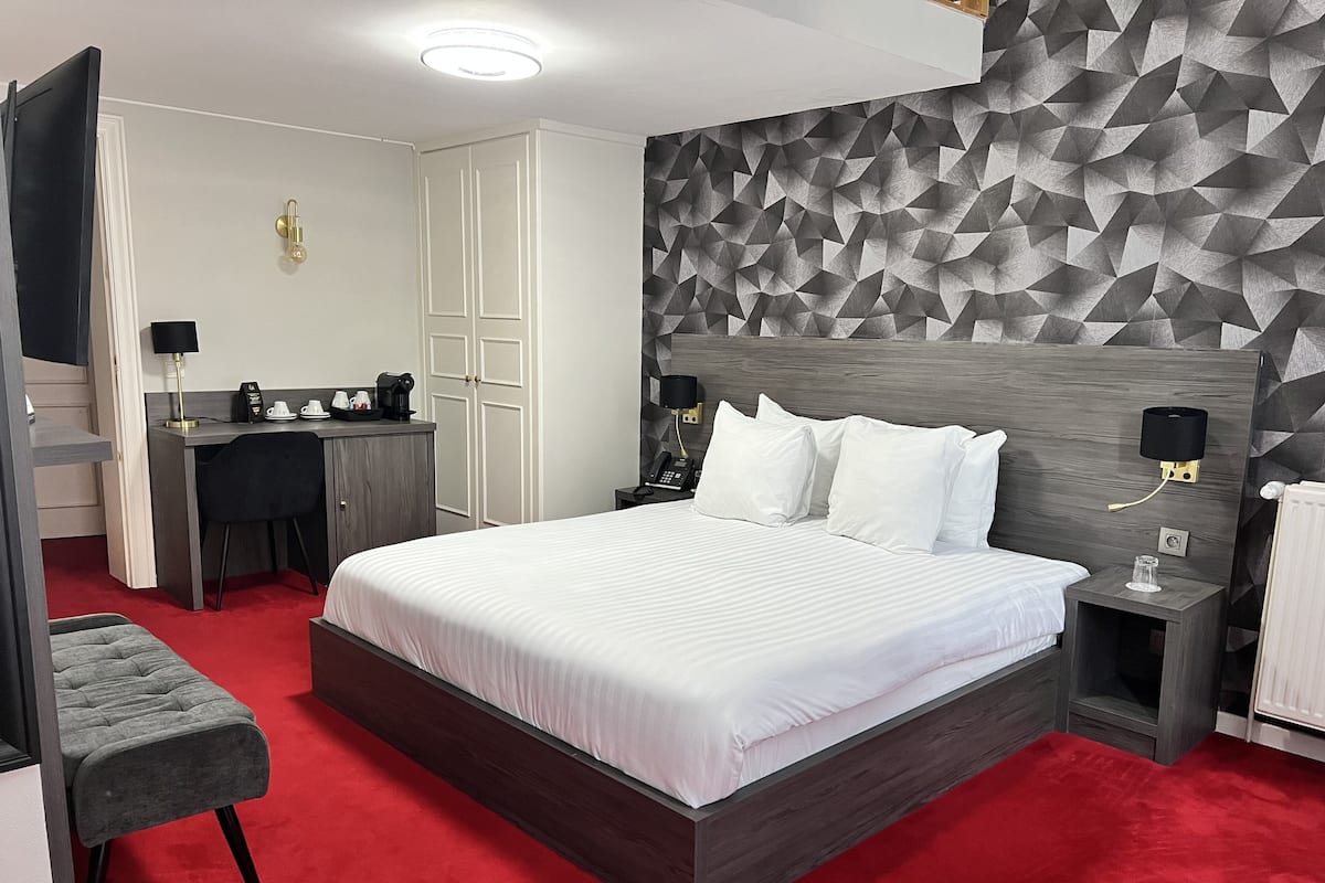 A modern hotel room with a large bed, a desk, and a wardrobe.