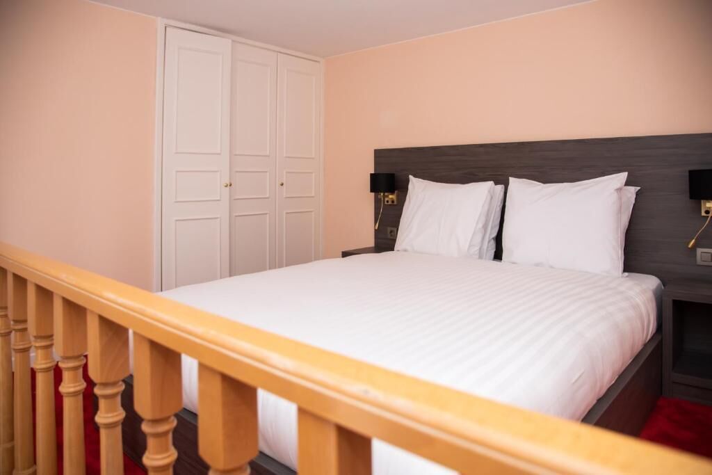 A hotel room with a bed, a wooden headboard, a nightstand with a lamp, and a wardrobe.