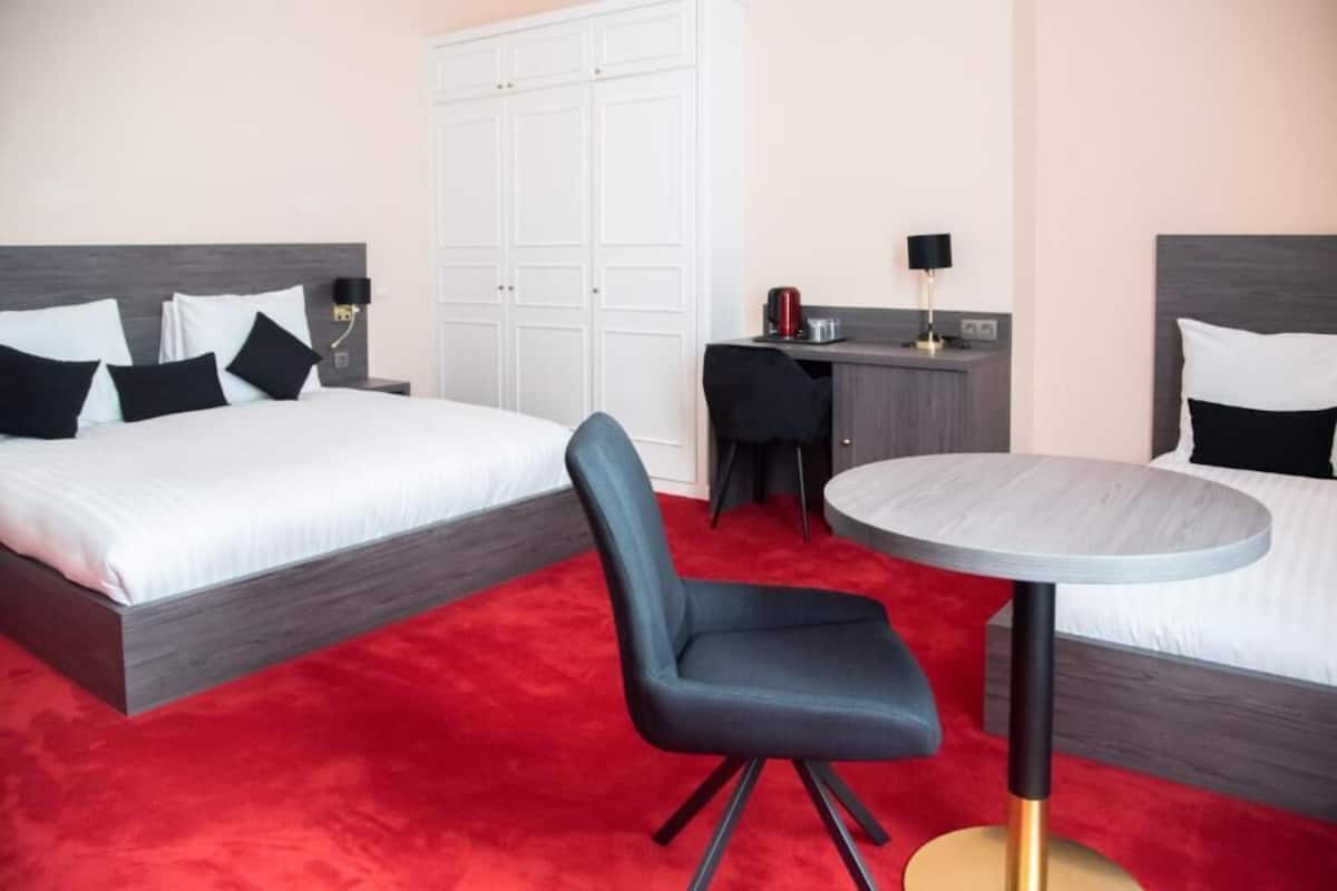 A hotel room with two beds, a desk, a chair, and a round table.