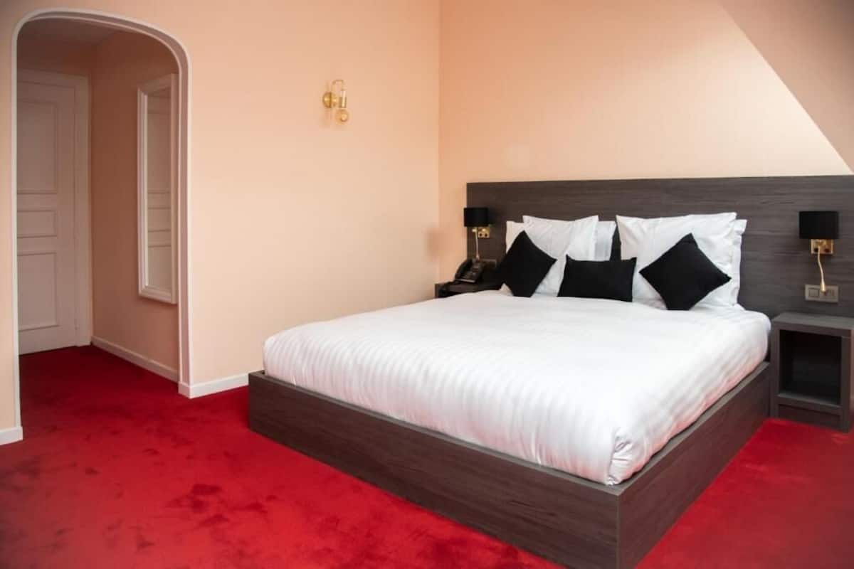 A bedroom with a large bed, a red carpet, a wooden headboard, and a nightstand with a lamp.