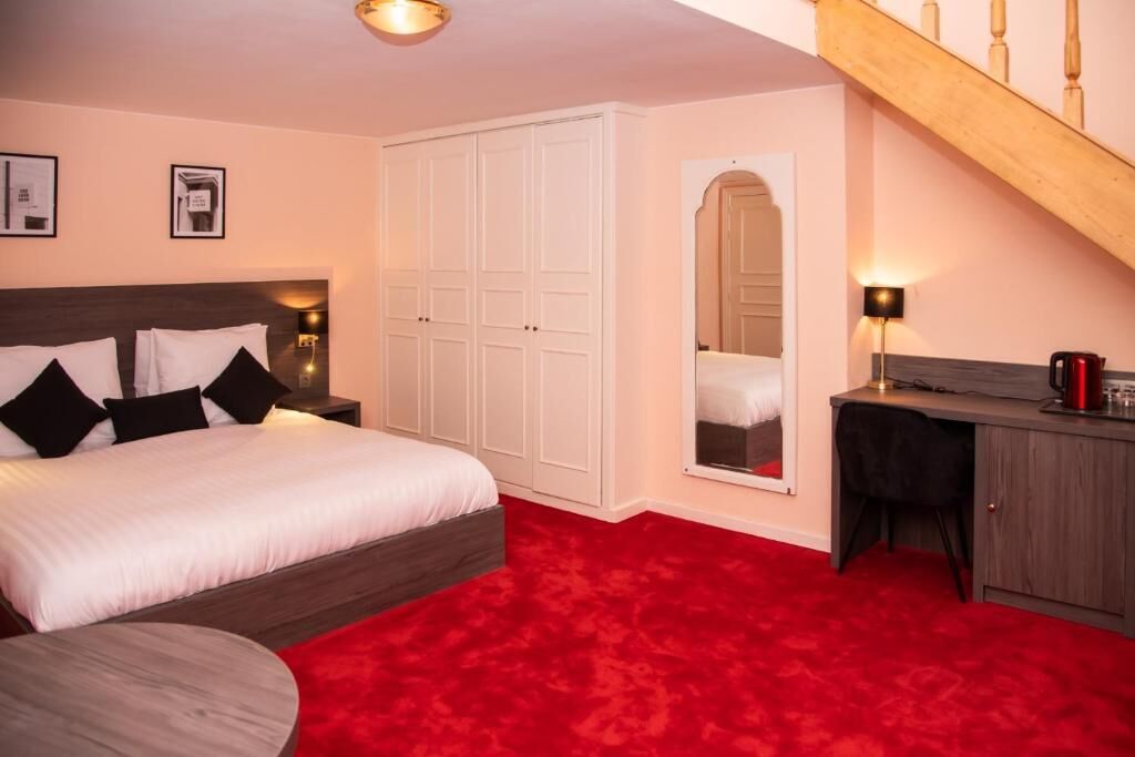 A bedroom with a large bed, a desk, a chair, a wardrobe, and a staircase.