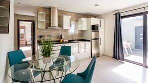 A modern kitchen with white cabinets, a stainless steel refrigerator, and a glass dining table with teal chairs. - Keito 2BR APT #K3-3 min to Palm Beach-Sleeps 4 (Noord)