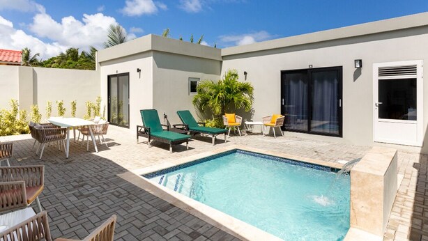 A modern outdoor pool area with lounge chairs, a table, and a small garden. - Keito 2BR APT #K3-3 min to Palm Beach-Sleeps 4 (Noord)