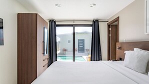 A modern hotel room with a large bed, a wooden wardrobe, a sliding glass door leading to a pool area, and a view of the outside. - Keito 2BR APT #K3-3 min to Palm Beach-Sleeps 4 (Noord)