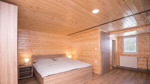 A wooden-paneled bedroom with a bed, bedside lamps, and a window. - Zotlar House (Bohinj)