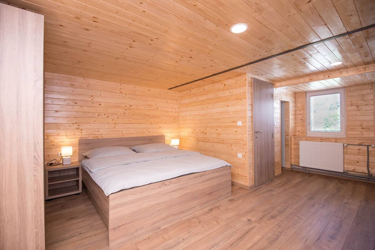 A wooden-paneled bedroom with a bed, bedside lamps, and a window.