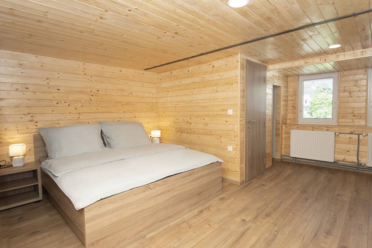 A wooden-paneled bedroom with a bed, bedside lamps, a radiator, and a window.