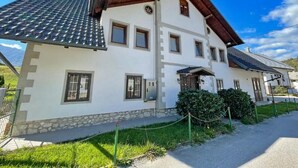 A two-story building with a tiled roof, stone base, and multiple windows. - Zotlar House (Bohinj)