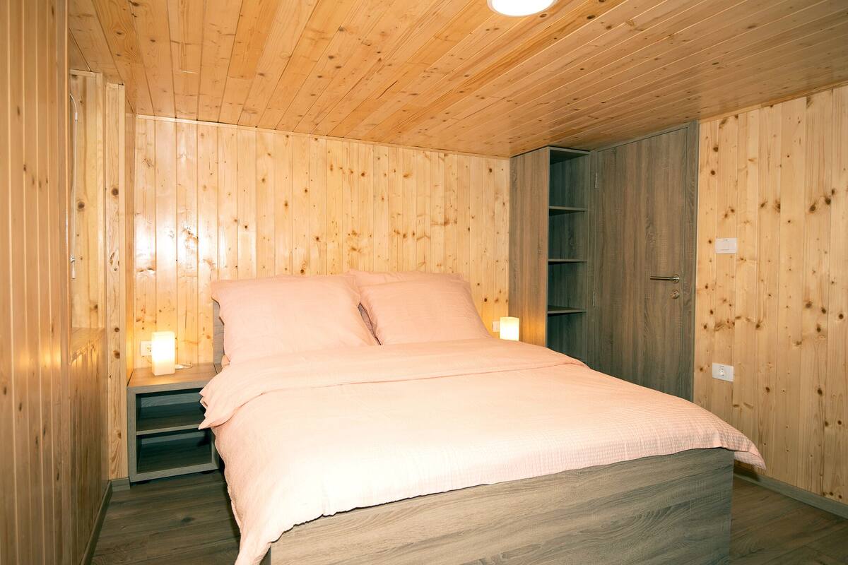 A wooden-paneled room with a bed, nightstands, and a wardrobe.