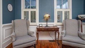 Una habitación con dos sillones, un escritorio de madera y dos ventanas con contraventanas.