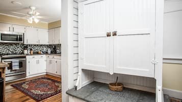 Une cuisine avec des meubles blancs, un four à micro-ondes et un ventilateur de plafond.