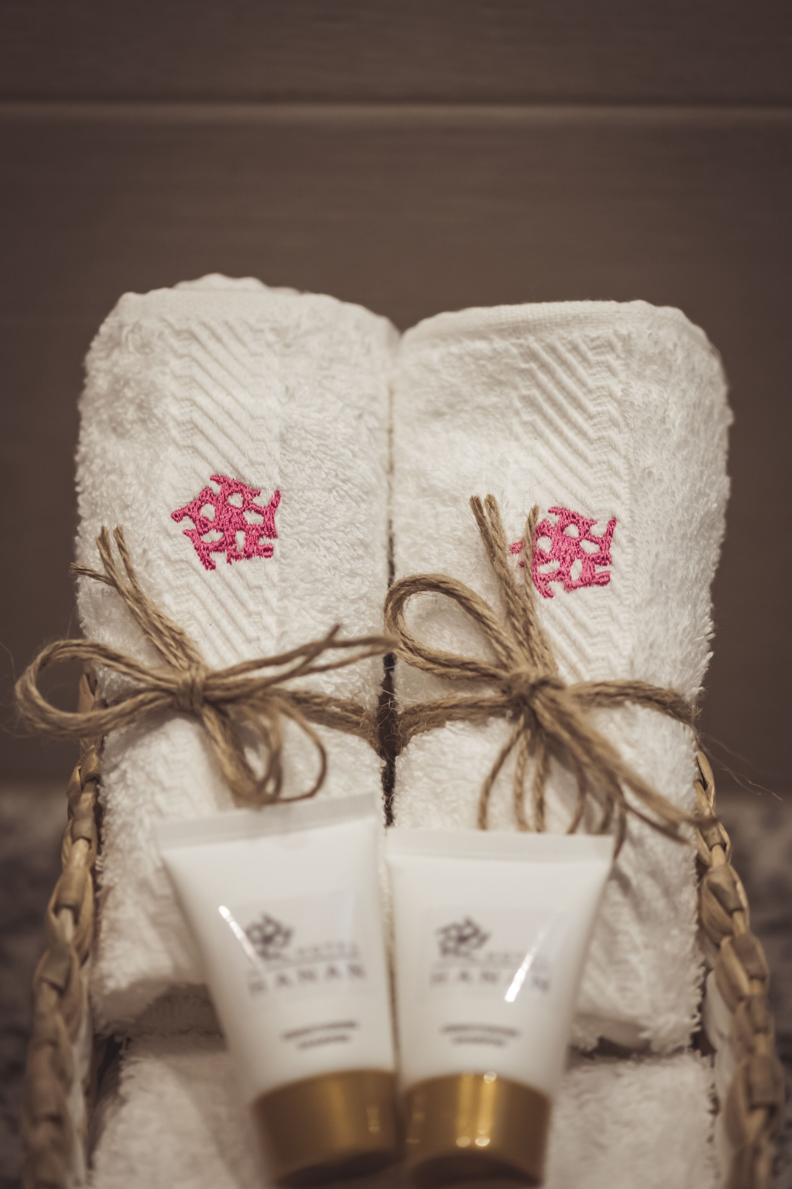 Un ensemble de serviettes blanches ornées de broderies roses, attachées avec de la ficelle, et deux tubes de crème.