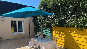 A patio with a table and chairs, a blue umbrella, and a yellow wall. - Charming gîte in Carantec, 44m² of happiness between sea, calm and barbecue! (Carantec)